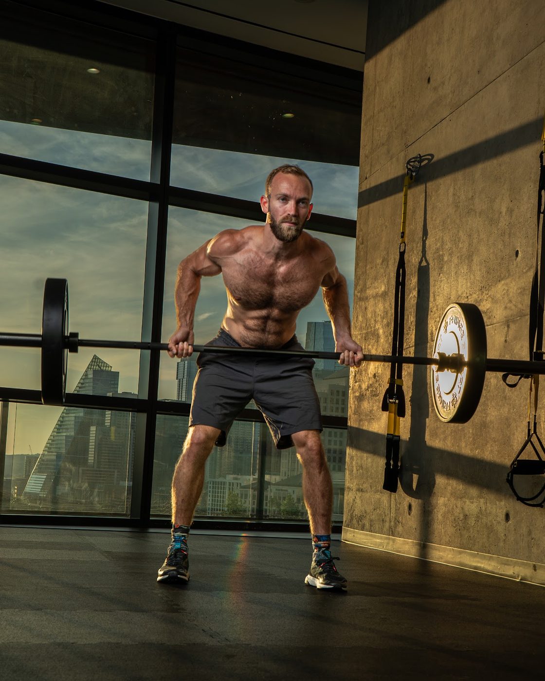Athlete lifting a barbell in a gym with the Austin skyline behind him