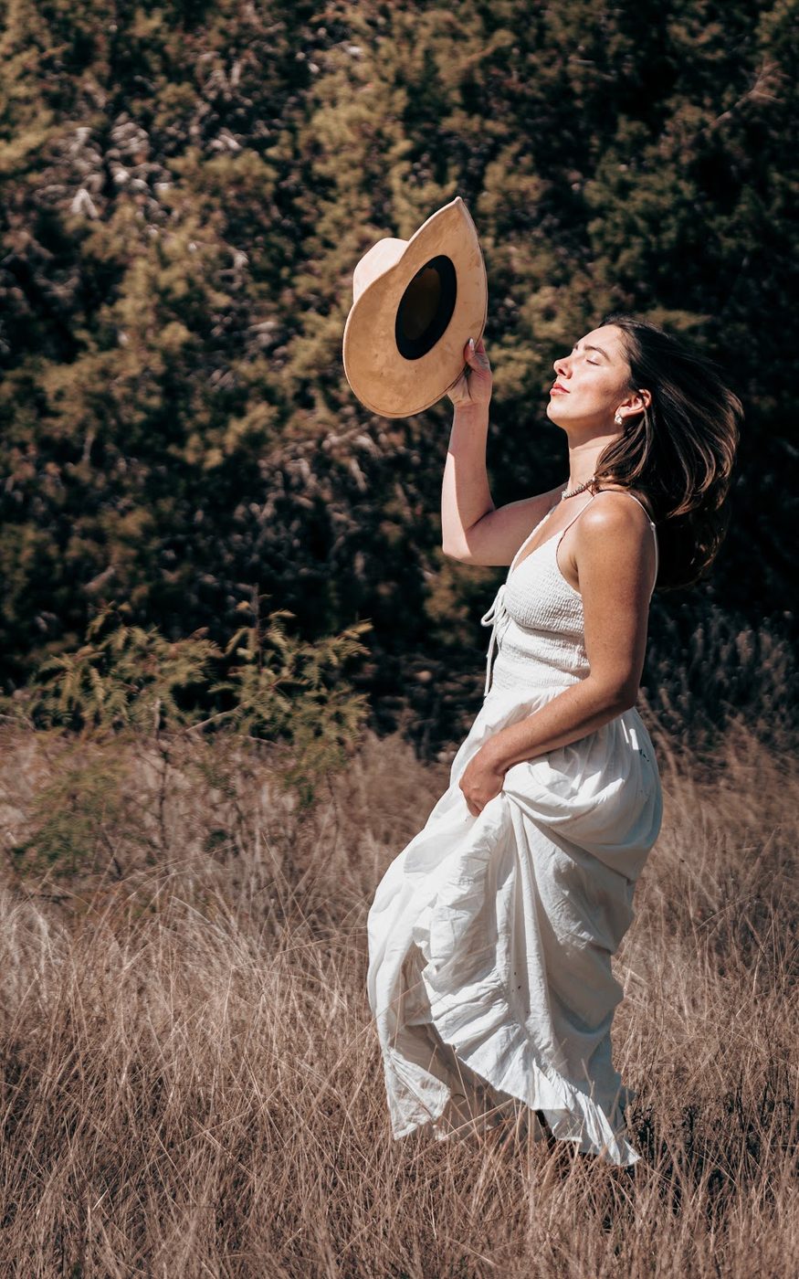 Woman in a white dress lifting her hat in a field