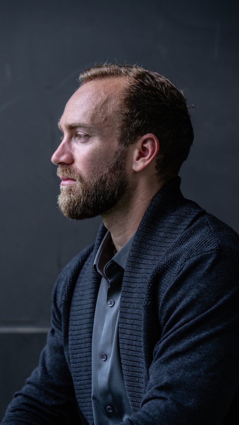 Profile headshot of a bearded man against a dark background